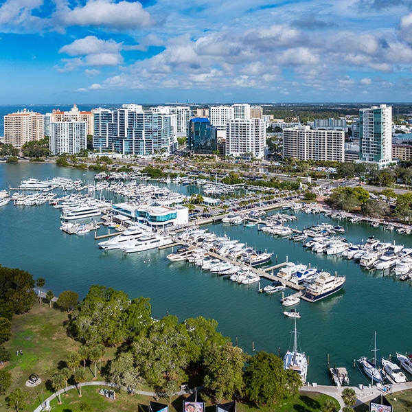 Aerial view of a marina with yachts and high-rise buildings under a blue sky.